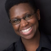Head and shoulders shot of Lenna who has dark brown skin and is wearing glasses and black shirt with collar